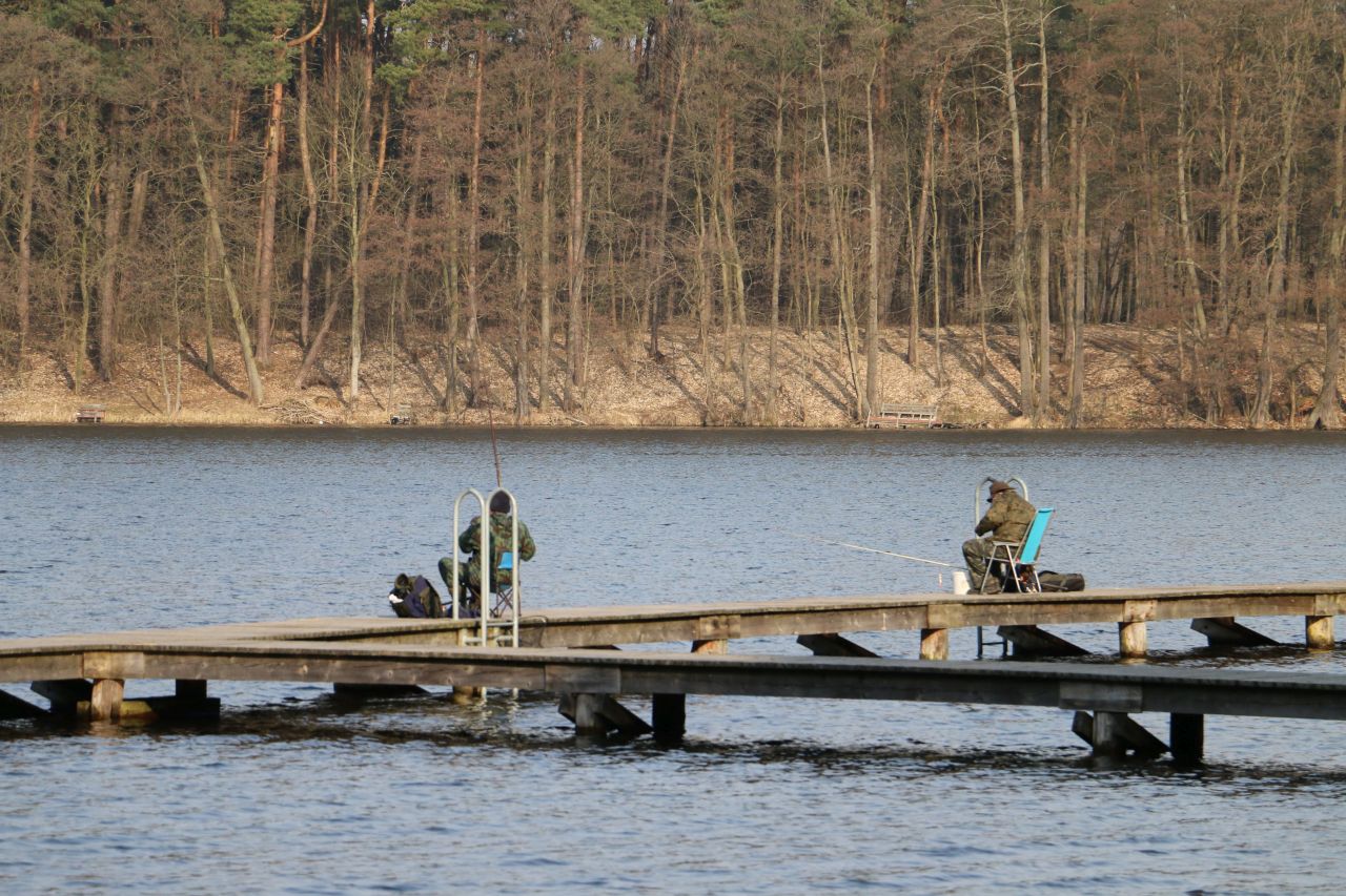 Zdjęcie dwóch wędkarzy siedzących na pomoście i łowiących ryby